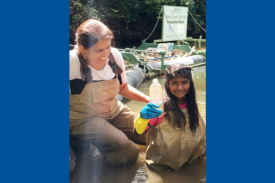 Surabhi Shah in a river with a child holding a plastic water bottle, conducting field work